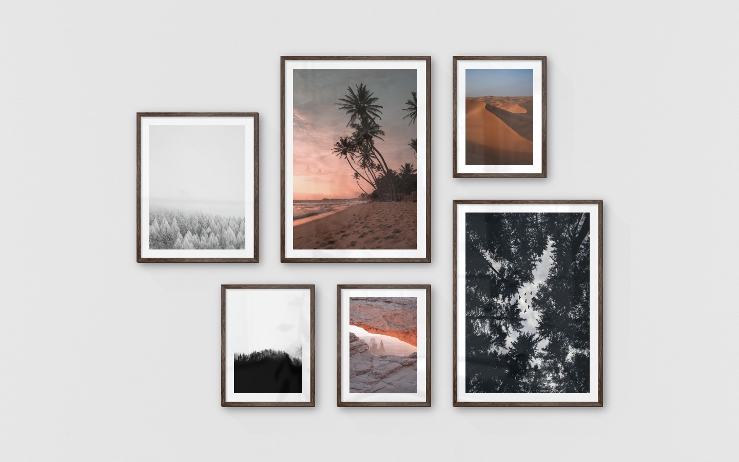Gallery wall with picture frames in dark wood in sizes 40x50, 50x70 and 30x40 with prints "Wooden tops in winter", "Beach at sunset", "Wooden tops and fog", "View between cliffs", "Wooden tops and birds" and "Desert"