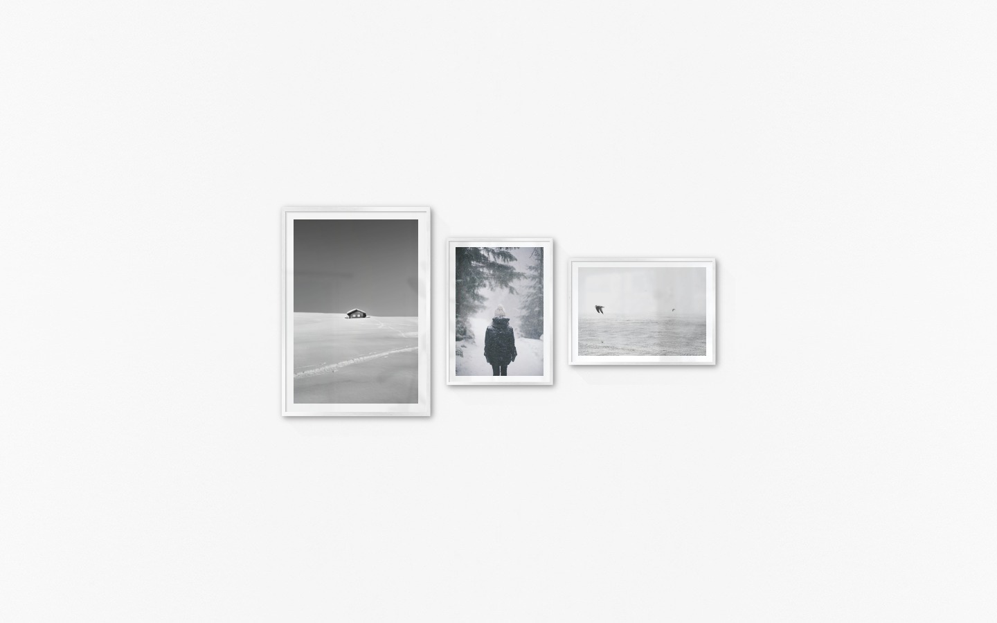 Gallery wall with picture frames in silver in sizes 70x100 and 50x70 with prints "Cottage in the snow", "Person in the snow" and "Birds over the sea"