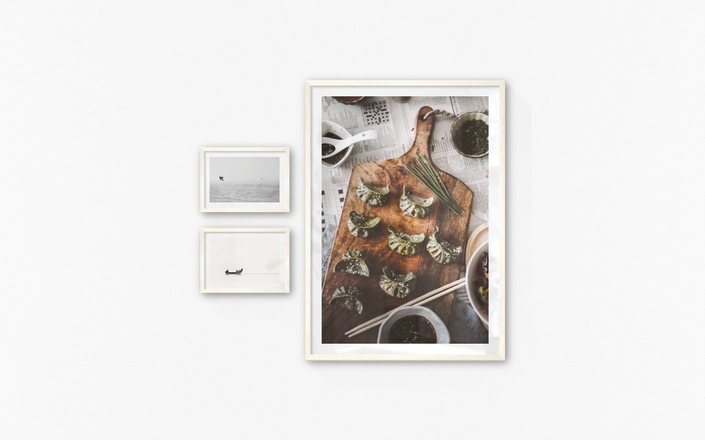 Gallery wall with picture frames in light wood in sizes 21x30 and 70x100 with prints "Birds over the sea", "People in boat" and "Dumplings"